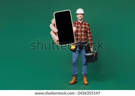 Full body young laborer man wear red shirt hardhat hat work hold toolbox blank screen mobile cell phone isolated on plain green background Instruments for renovation apartment room Repair home concept