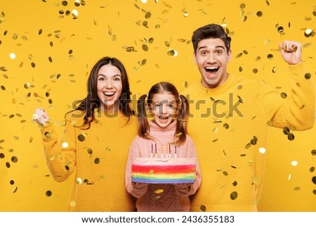 Young overjoyed happy parents mom dad with child kid girl 7-8 years old wear pink sweater casual clothes hold birthday cake do winner gesture isolated on plain yellow background. Family day concept