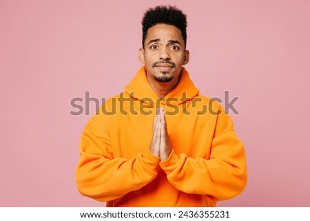 Young man of African American ethnicity wear yellow hoody casual clothes hold hands folded in prayer gesture, begging about something isolated on plain pastel light pink background. Lifestyle concept Royalty-Free Stock Photo #2436355231