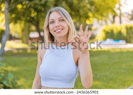 Young blonde woman at outdoors showing ok sign with fingers