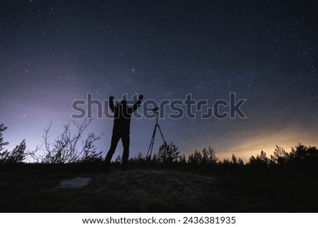 Happy male landscape astrophotographer with a camera on a tripod outdoors in early spring at night under the starry sky.  Royalty-Free Stock Photo #2436381935