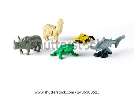 animals figures toys in a white background, rhinoceros, llama, green frog, yellow salamander and hammerhead shark