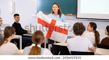 High school teacher holds the flag of England in her hands and talks about this country in a geography lesson