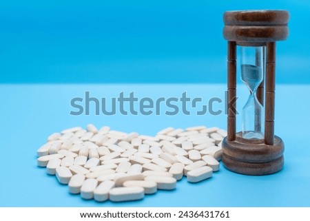 Pills forming a heart together with an hourglass. concept of taking care of your health, self-love, self-esteem, daily dose, isolated on blue background with copy space Royalty-Free Stock Photo #2436431761