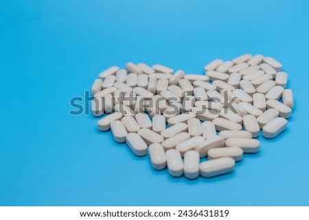 Front view pills forming a heart, concept of taking care of your health, self-love, self-esteem, daily dose, isolated on blue background with copy space Royalty-Free Stock Photo #2436431819