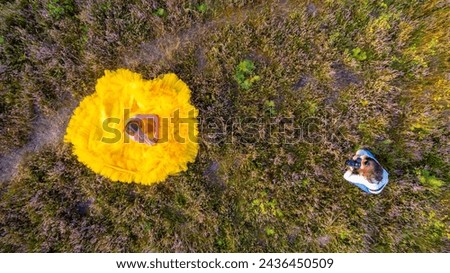 From an aerial viewpoint, a woman in a billowing yellow dress is centered like a blooming flower against the textured greens and purples of a natural landscape. Aerial Bloom: Woman in a Yellow Dress