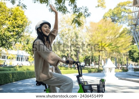 Young beautiful Asian woman in safe bike helmet and protective exercises in riding using electric bicycle in a city park.