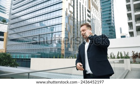 Skilled businessman talking to marketing team about marketing strategy by using phone while standing at skyscraper. Happy manager calling colleague about increasing sales at modern urban city. Urbane.
