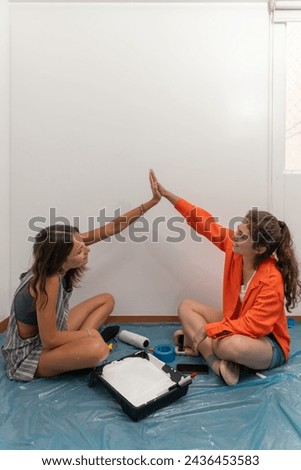 Vertical photo of two female friends clasping hands while painting the new apartment Royalty-Free Stock Photo #2436453583
