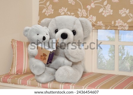 Parent and child teddy bears reading a book, sitting on a bench in front of picture window