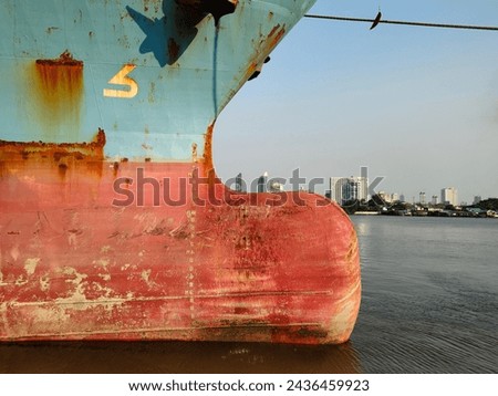 Anchor on large cargo ship's anchor being pulled. Blue and red ship, While docked at the pier by large ropes on the river, in the background is a view of the city's buildings and transport concept