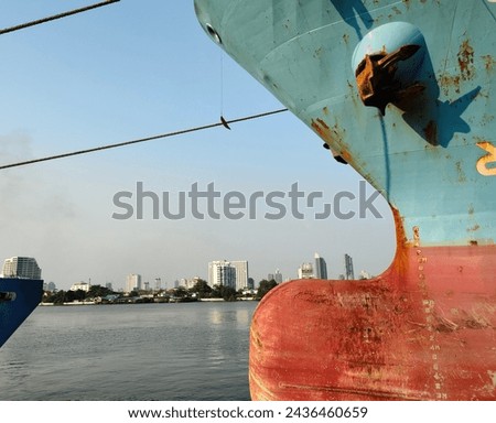 Anchor on large cargo ship's anchor being pulled. Blue and red ship, While docked at the pier by large ropes on the river, in the background of the river, city's buildings view and transport concept