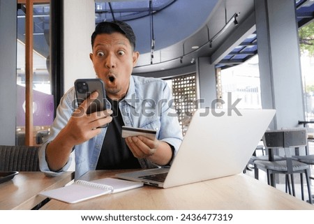 Asian man using laptop and mobile phone for shopping online with credit card in coffee shop online freelance business
