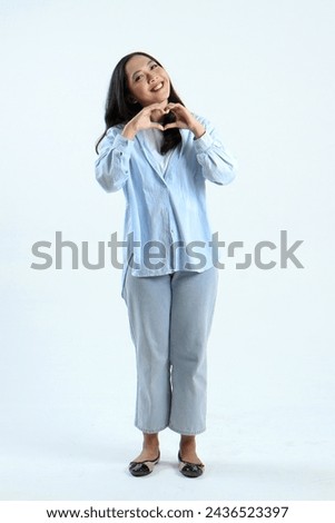 full leght shoot of happy asian Indonesian woman wearing casual attire, showing love sign gesture on isolated background