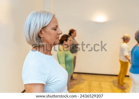 Side view of a mature woman closing eyes breathing during a qigong class next to other participants Royalty-Free Stock Photo #2436529207