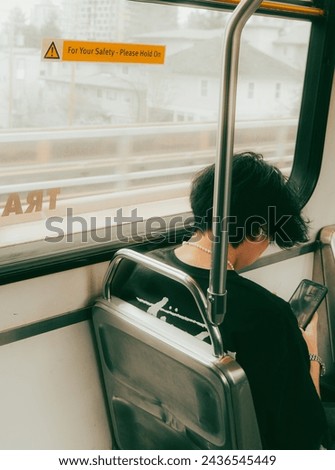 Stay connected on the go with this photo of a person engrossed in their phone while riding the skytrain. Capture the essence of modern commuting and technology in this dynamic image.