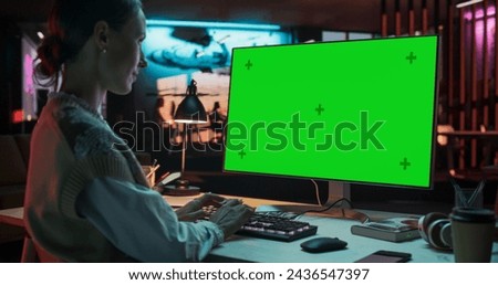 Over the Shoulder: Young Woman Sitting at Her Desk Using Desktop Computer with Mock-up Green Screen. Female Caucasian Specialist Working on Computer with Chroma Key Display at Creative Agency