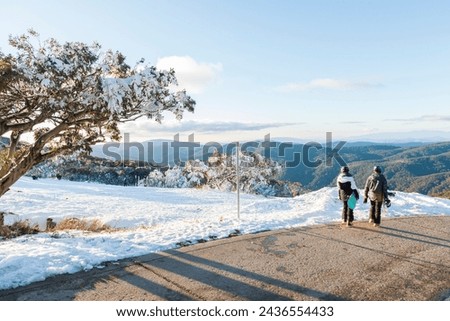 Mount Buller in Victoria, Australia. A pair of snowboarders walk across the snow to admire the view of the mountain.  Royalty-Free Stock Photo #2436554433