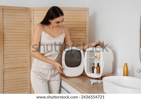Beautiful young happy woman with small refrigerator for cosmetic products in bathroom