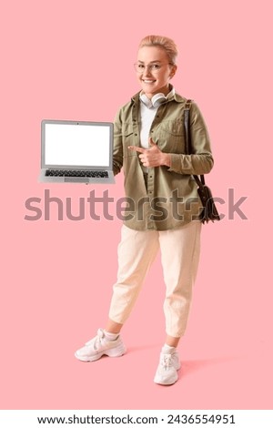 Young woman pointing at laptop on pink background