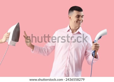 Happy young man choosing modern steamer over electric iron on pink background