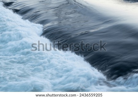 Rapid water flow over barrier, river overflow over dam close up with splash and foam, abstract landscape pastel blue Royalty-Free Stock Photo #2436559205