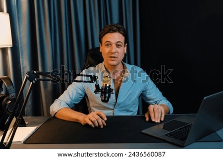 Host channel smart broadcaster talking on live social media application searching on laptop, broadcasting streamer wearing headphone using mic at modern home office studio in warm lighting. Pecuniary.
