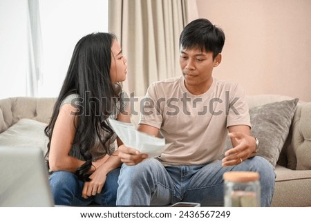 An unhappy and stressed Asian wife is arguing with her husband about unexpected expenses and high domestic bills on the sofa in the living room. spouses quarreling at home. family bankruptcy Royalty-Free Stock Photo #2436567249