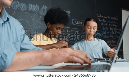 Young student fixing controller while teacher programing engineering code at STEM class. Closeup of instructor hand typing computer while smart girl using electronic tool and blackboard. Edification.