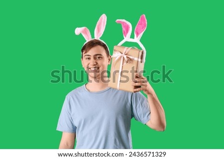 Happy young man in bunny ears with gift box on green background. Easter celebration