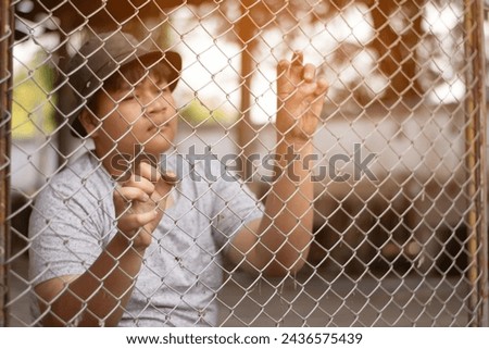 Asian teenboy sitting and holding big metal fence panel in front of a juvenile detention facility, awaiting further release with friends sadly, freedom and detention of people concept. Royalty-Free Stock Photo #2436575439