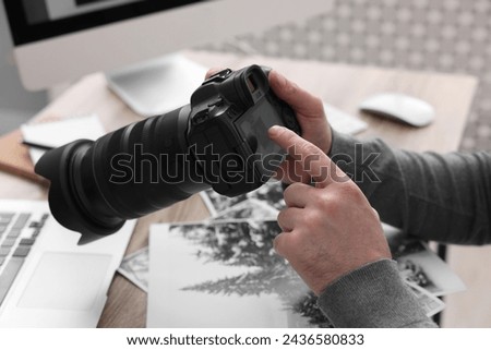 Professional photographer with digital camera at table indoors, closeup