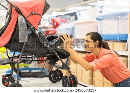 Mother woman carefully examines a modern, decision making stroller in spacious baby store, mindful parent, seeking quality and safety in children products family planning, baby care products, shopping Royalty-Free Stock Photo #2436590237