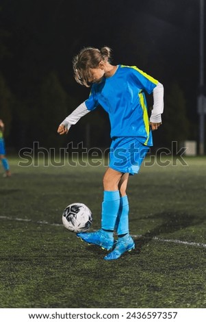 young girl wearing light blue uniform practicing soccer at night. High quality photo