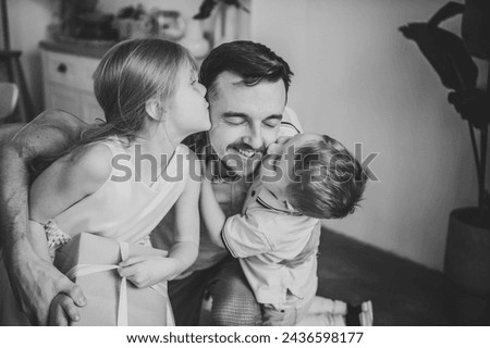 Children kissing, hugging, greeting happy father closeup. Child congratulate daddy. Daughter embraces smiling dad and gives present box gift. Son makes surprise for Fathers Day. Black and white photo