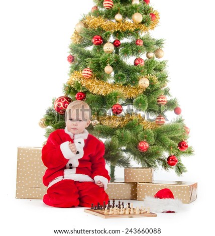 child dressed as a gnome play chess near a christmas tree and gift box.
