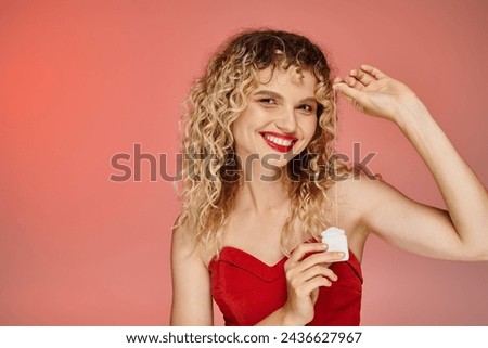portrait of woman with wavy hair and red lips showing dental floss on pink gradient backdrop