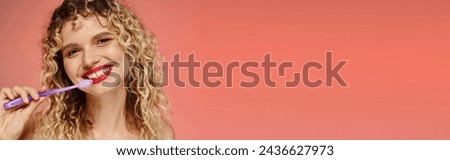 pretty curly woman with red lips and radiant smile cleaning teeth on pastel pink backdrop, banner