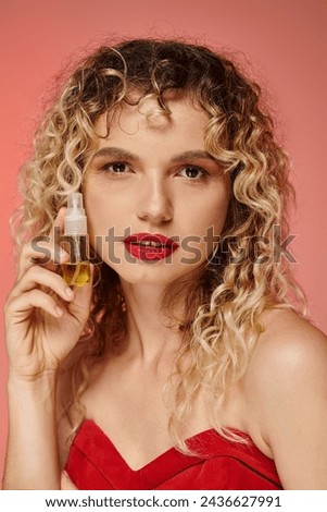 attractive woman with wavy hair and perfect skin showing perfume on pink and yellow backdrop