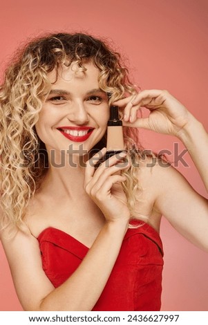 cheerful pretty woman with curly hair and perfect skin showing makeup foundation on pink backdrop