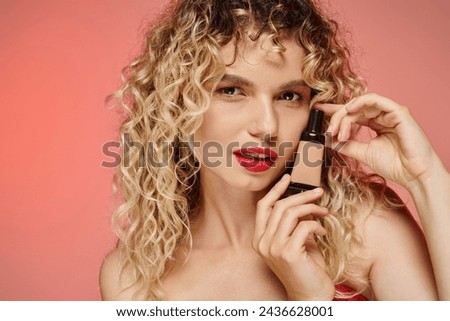 mesmerizing woman with red lips and wavy hair showing makeup foundation on pastel pink backdrop
