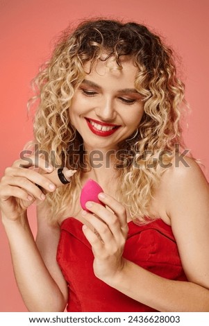 smiling trendy woman applying makeup foundation on cosmetic sponge on pink and yellow backdrop