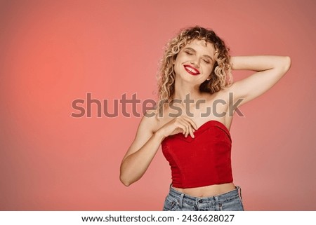 trendy woman with bold makeup in red top smiling with closed eyes on pink and yellow pastel backdrop
