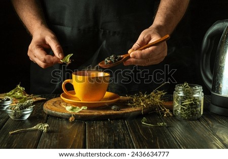 A man brews healthy tea from medicinal dry herbs. A hand holds a spoon with dry rose hips to add to a cup. Traditional medicine concept. Royalty-Free Stock Photo #2436634777