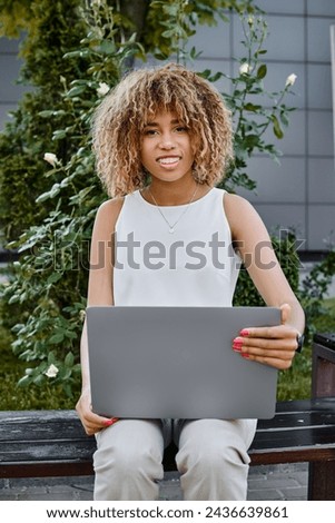 happy curly african american freelancer using her laptop and sitting on bench, career woman