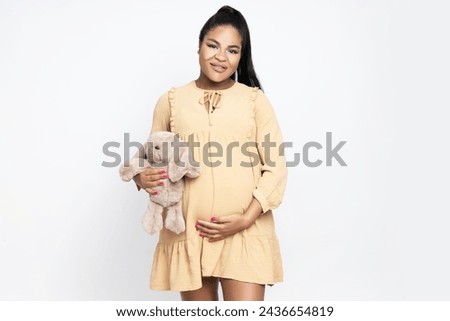 A pregnant African-American woman, in a dress, on a light background.