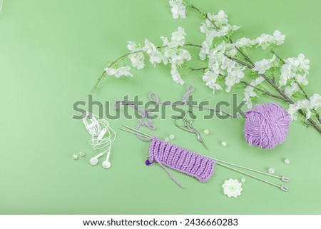 Spring knitting concept. Pattern example, traditional tools, ball of yarn, blooming cherry branch. Creative handmade flat lay, pastel green background, top view