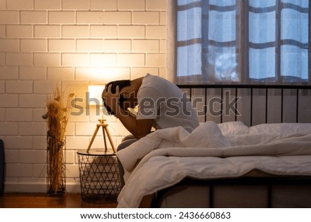 Asian frustrated insomnia man in pajamas sit on bed in dark night time. Attractive depressed young sleepless man feeling upset, worried and concerned cannot sleep from nightmare in bedroom in home. Royalty-Free Stock Photo #2436660863