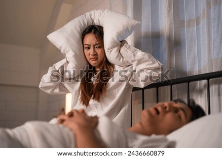 Asian woman feel frustrated from husband snoring while sleep at night. Attractive insomnia angry wife sitting on bed, cannot sleep due to noise and put cozy blanket on her ears in bedroom at home.
 Royalty-Free Stock Photo #2436660879