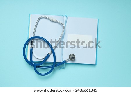 Notepad and stethoscope on blue background, top view